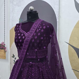Puede incluir: Un lehenga de lentejuelas morado con un choli a juego. El lehenga tiene un patr&oacute;n de chevron y el choli tiene un patr&oacute;n de diamante. El atuendo est&aacute; decorado con lentejuelas plateadas.