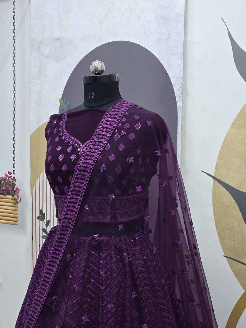 Puede incluir: Un lehenga de lentejuelas morado con un choli a juego. El lehenga tiene un patr&oacute;n de chevron y el choli tiene un patr&oacute;n de diamante. El atuendo est&aacute; decorado con lentejuelas plateadas.