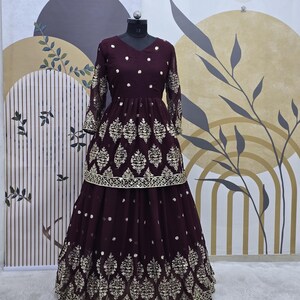 May include: A maroon-colored dress with gold embroidery and sequins. The dress has a fitted bodice and a flowing skirt. The skirt is layered and has a gold trim.