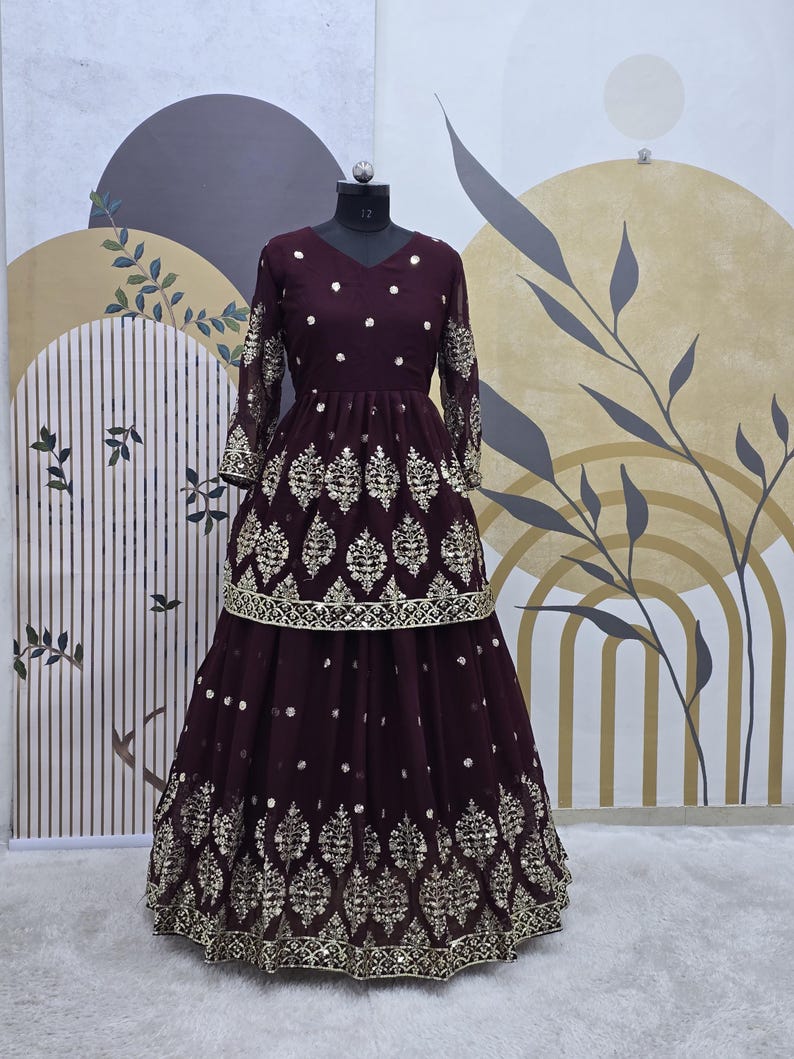 May include: A maroon-colored dress with gold embroidery and sequins. The dress has a fitted bodice and a flowing skirt. The skirt is layered and has a gold trim.