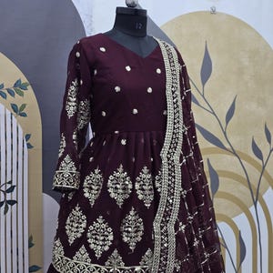 May include: A maroon long-sleeved dress with silver embroidery and a matching dupatta. The dress has a flared skirt and a fitted bodice. The dupatta is decorated with sequins and has a scalloped border.