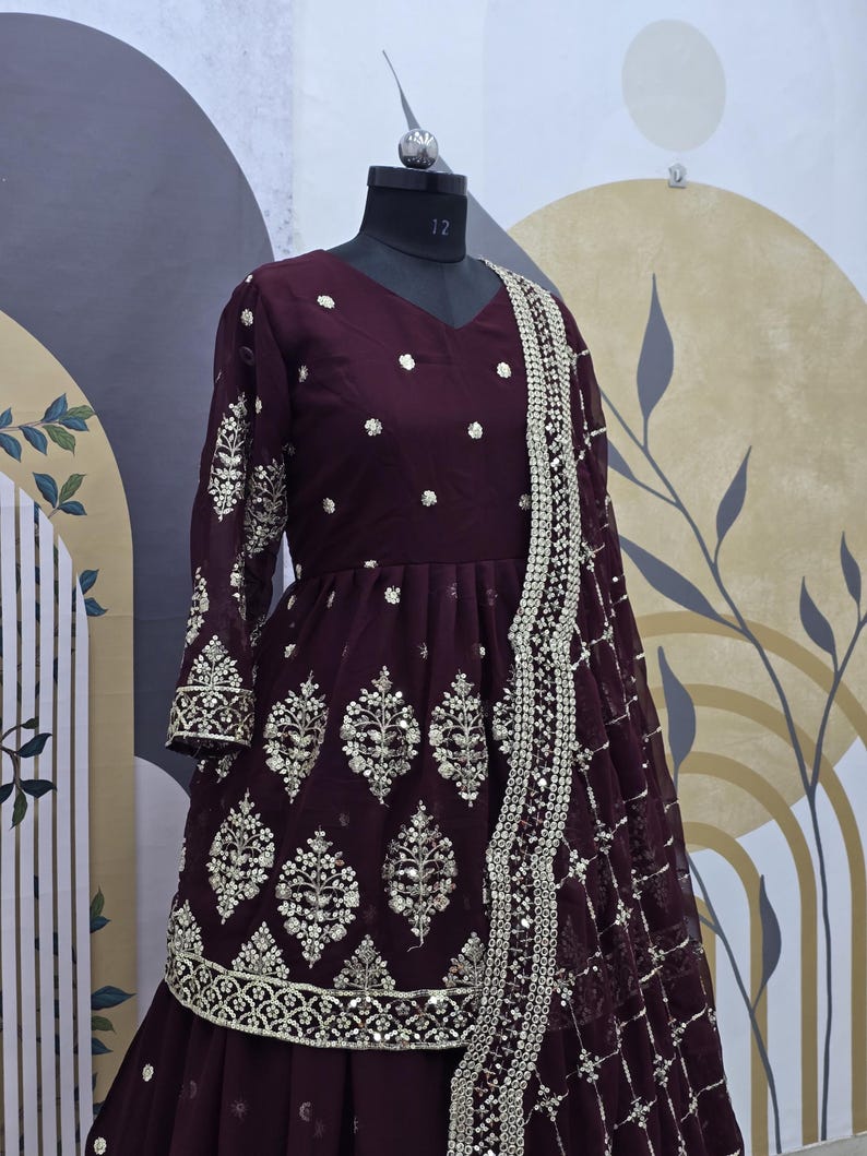 May include: A maroon long-sleeved dress with silver embroidery and a matching dupatta. The dress has a flared skirt and a fitted bodice. The dupatta is decorated with sequins and has a scalloped border.