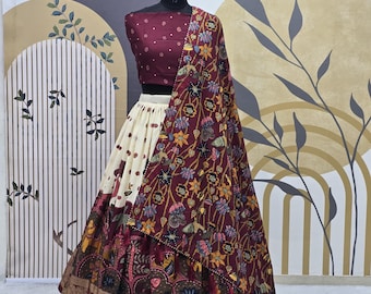 Puede incluir: Un atuendo de novia indio en color marrón y blanco con un dupatta de estampado floral. La falda es blanca con ribete marrón y la blusa es marrón con estampado floral. El dupatta es marrón con estampado floral y tiene un borde dorado.