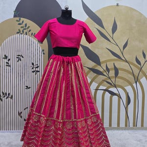 Pode incluir: Um lehenga bordado em rosa e dourado com um top curto combinando. A saia apresenta um design em camadas com lantejoulas douradas e trabalho de espelho.