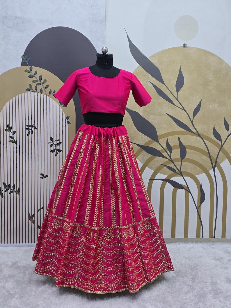 Pode incluir: Um lehenga bordado em rosa e dourado com um top curto combinando. A saia apresenta um design em camadas com lantejoulas douradas e trabalho de espelho.