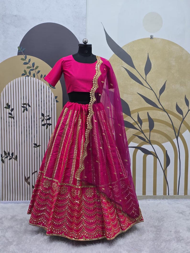 Pode incluir: Um lehenga bordado em rosa e dourado com um choli combinando. O lehenga tem uma saia rodada com uma borda dourada e bordados intrincados. O choli tem um decote redondo e mangas curtas. O dupatta &eacute; um tecido transparente com uma borda dourada.