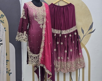 May include: A formal, two-piece outfit in shades of burgundy and pink. The ensemble includes a long-sleeved top with intricate gold embroidery and matching pants. A flowing pink scarf and a wide-legged skirt with gold embellishments complete the look.