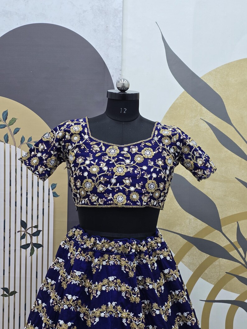 May include: A blue and gold embroidered crop top and skirt set. The top has short sleeves and a round neckline. The skirt is full length and has a gathered waist.