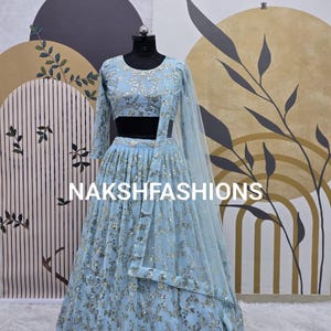 Puede incluir: Un lehenga bordado de color azul claro con un top corto a juego y una dupatta transparente. El atuendo está decorado con lentejuelas plateadas y presenta un diseño floral.
