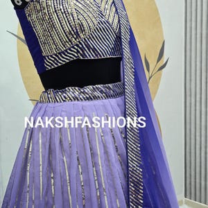 Op de afbeelding: Een paars en blauwe set met een crop top en rok met een bijpassende dupatta. De top heeft een V-hals en de rok is een vloeiende A-lijn stijl. De set is versierd met zilveren pailletten.