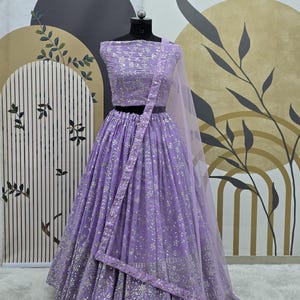 Op de afbeelding: Een lavendelkleurige lehenga met zilveren borduurwerk en pailletten. De rok is vol en zwierig, en het topje is strak. De dupatta is doorschijnend en heeft een delicaat bloemenpatroon.