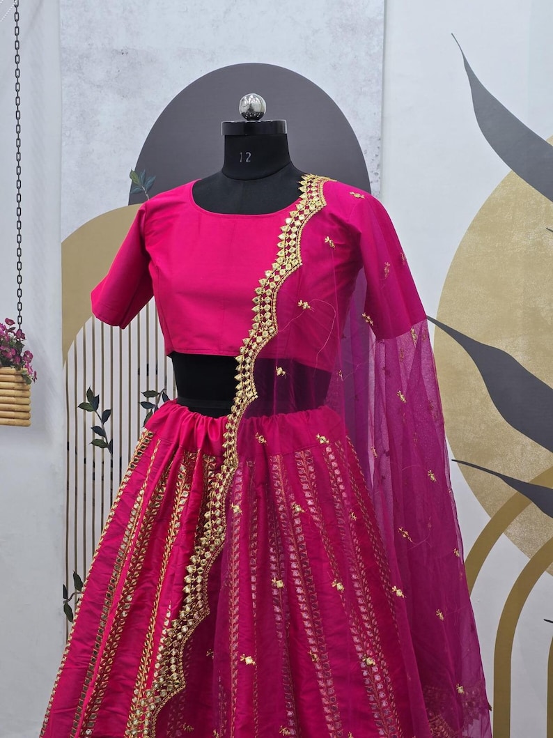Pode incluir: Um lehenga magenta com bordados dourados e lantejoulas. A saia &eacute; feita de um tecido transparente com um dupatta magenta combinando.