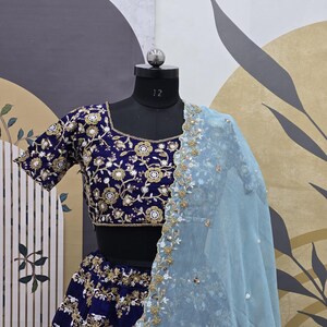 May include: A dark blue embroidered lehenga with a matching choli and a light blue dupatta. The choli has a floral design with gold and white embellishments. The lehenga and dupatta are also embroidered with gold and white thread.