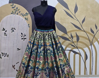 May include: A blue and gold brocade skirt with a floral pattern. The skirt is paired with a navy blue crop top with a one-shoulder design.