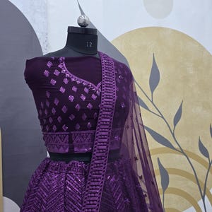 Puede incluir: Un conjunto de top corto y falda de color morado bordado y con lentejuelas, con una dupatta transparente a juego. El atuendo presenta intrincados patrones geom&eacute;tricos y un delicado dise&ntilde;o floral.