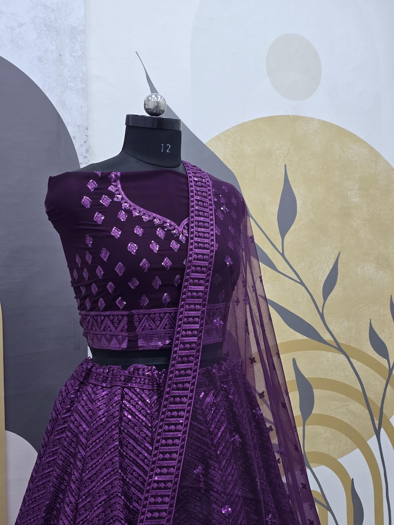 Puede incluir: Un conjunto de top corto y falda de color morado bordado y con lentejuelas, con una dupatta transparente a juego. El atuendo presenta intrincados patrones geom&eacute;tricos y un delicado dise&ntilde;o floral.