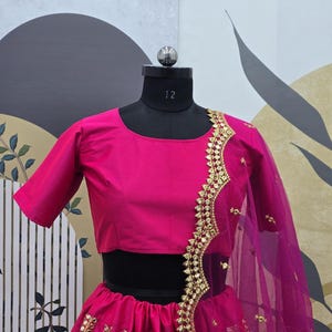 Pode incluir: Um lehenga bordado em rosa e dourado com uma blusa rosa combinando. O lehenga tem uma saia rodada com uma borda dourada e um dupatta combinando.