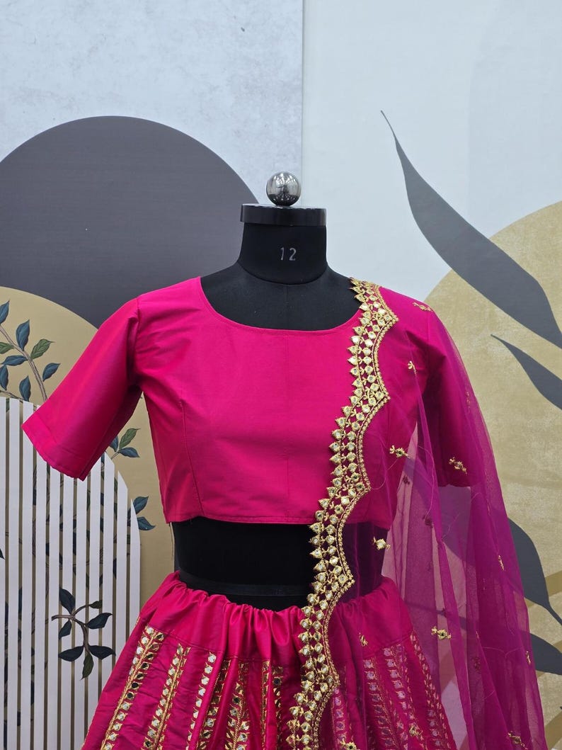 Pode incluir: Um lehenga bordado em rosa e dourado com uma blusa rosa combinando. O lehenga tem uma saia rodada com uma borda dourada e um dupatta combinando.