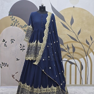 Puede incluir: Un vestido formal azul marino con adornos dorados. El vestido presenta una falda larga, un corpiño ajustado con detalles de botones y mangas tres cuartos. Una chal a juego con ribete dorado está drapeado sobre el maniquí.