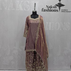 May include: A mauve-colored three-piece outfit on a mannequin, featuring a square-neck tunic with gold embroidery, wide-leg pants with intricate gold floral patterns, and a matching sheer dupatta with a gold border, labeled Naksh fashions.