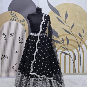 May include: A black net lehenga with silver embroidery and sequins. The lehenga has a scalloped hemline and a matching black crop top.