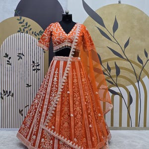 May include: An orange and white embroidered lehenga with a matching choli. The lehenga has a flared skirt with a net dupatta.