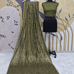 May include: A green sequined saree with a matching green sequined blouse. The saree is draped over a mannequin and the blouse is displayed on a separate mannequin.