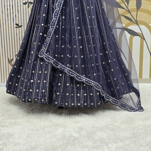 May include: A navy blue formal dress with silver dot and stripe embellishments. The dress features a flowing skirt and a matching sheer shawl with a scalloped edge. The fabric has a subtle sheen, and the design is elegant.