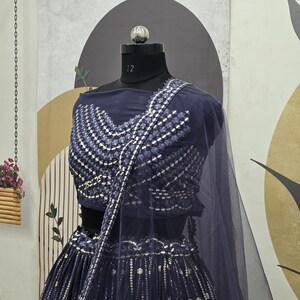 May include: A navy blue formal dress with intricate silver embroidery. The dress features a fitted bodice and a flowing skirt, with a matching sheer shawl. The ensemble is displayed on a mannequin, showcasing the detailed design and elegant style.