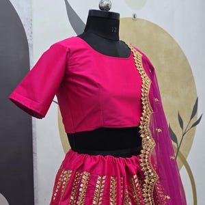 Pode incluir: Um lehenga bordado em rosa e dourado com um top curto rosa correspondente. A saia apresenta um padr&atilde;o vertical de lantejoulas douradas e trabalho de espelho. O dupatta &eacute; um tecido rosa transparente com bordados dourados.