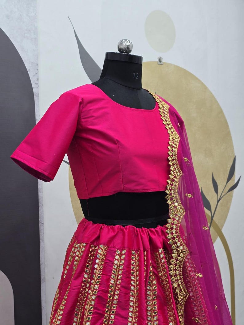 Pode incluir: Um lehenga bordado em rosa e dourado com um top curto rosa correspondente. A saia apresenta um padr&atilde;o vertical de lantejoulas douradas e trabalho de espelho. O dupatta &eacute; um tecido rosa transparente com bordados dourados.