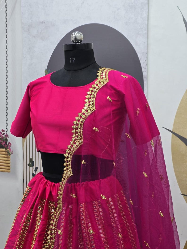 Pode incluir: Um lehenga bordado em rosa e dourado com um choli e um dupatta combinando. O lehenga tem uma saia rodada com bordados intrincados e uma borda dourada. O choli &eacute; um top curto sem mangas com um design de bordado semelhante. O dupatta &eacute; um tecido transparente com uma borda dourada.