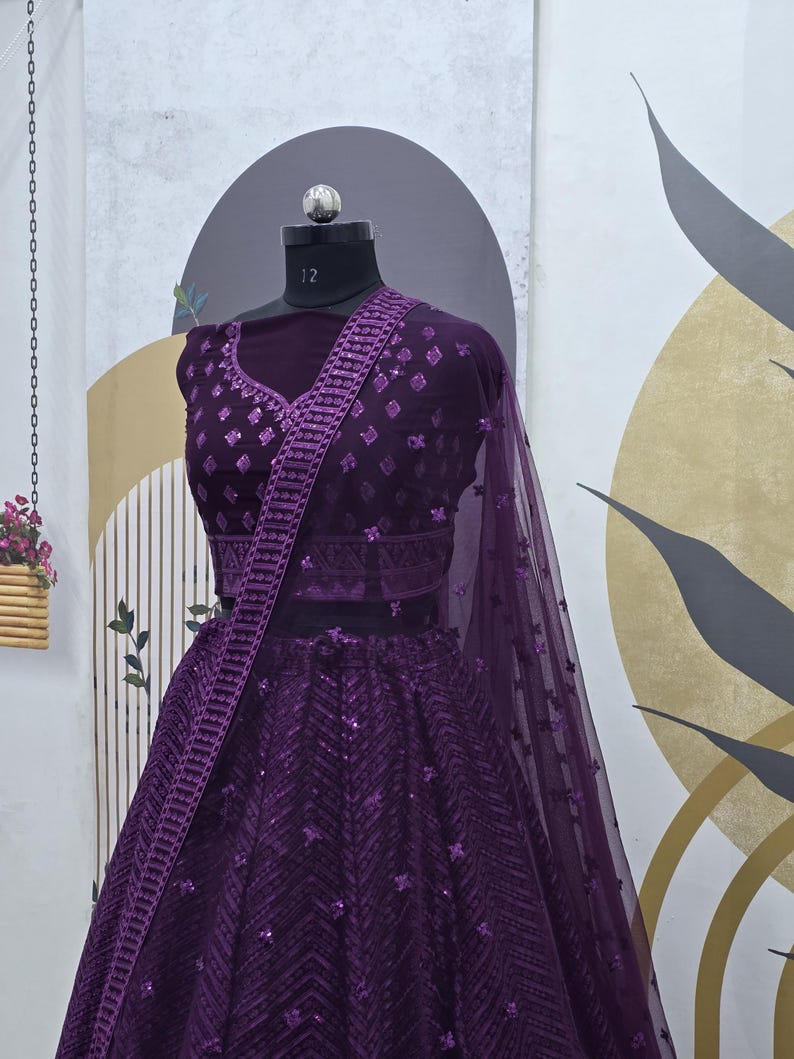 Puede incluir: Un lehenga bordado de color morado con un choli a juego. El lehenga est&aacute; hecho de tela de red con lentejuelas y un patr&oacute;n de chevron. El choli tiene un escote en V profundo y es sin mangas.