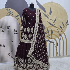 May include: A maroon-colored dress with gold embroidery and sequins. The dress has a long skirt and a fitted bodice. The dress is on a mannequin and has a matching dupatta.