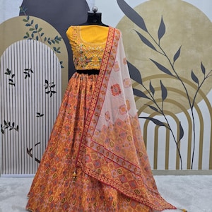 May include: A yellow and orange printed lehenga with a white dupatta. The lehenga features a floral print and the dupatta has a geometric pattern. The outfit is ideal for a special occasion.
