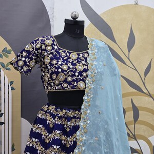 May include: A blue and gold embroidered lehenga with a matching blue and gold embroidered choli. The lehenga has a light blue sheer dupatta with gold embroidery.