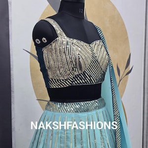 Op de afbeelding: Een lichtblauwe en groene set met een geknipt topje en rok met een zwarte buste. De rok heeft verticale strepen van pailletten en het topje heeft een sweetheart-halslijn. De tekst "NAKSHFASHIONS" is zichtbaar op de rok.