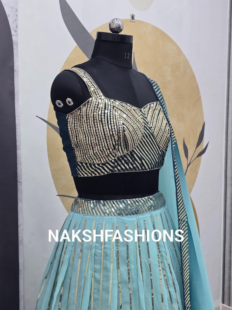 Op de afbeelding: Een lichtblauwe en groene set met een geknipt topje en rok met een zwarte buste. De rok heeft verticale strepen van pailletten en het topje heeft een sweetheart-halslijn. De tekst "NAKSHFASHIONS" is zichtbaar op de rok.