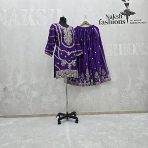 Peut inclure: Une tenue violette brod&eacute;e, compos&eacute;e d'un haut &agrave; manches longues et d'une jupe, pr&eacute;sent&eacute;e sur un mannequin et un cintre. La tenue pr&eacute;sente des broderies dor&eacute;es complexes. La marque "Naksh fashions" est visible en arri&egrave;re-plan.