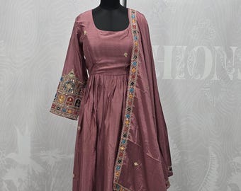 May include: A mauve floor-length dress with a scoop neckline and three-quarter sleeves. The cuffs and hem feature intricate embroidery with mirrors and colorful accents. A matching dupatta with a decorative border is draped over the shoulder.