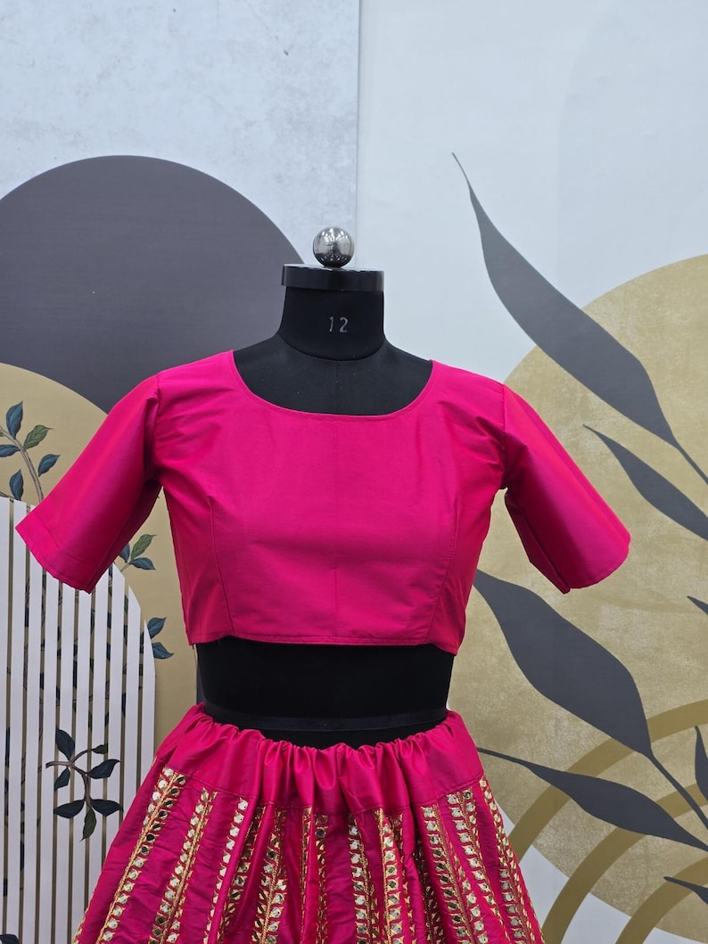 Pode incluir: Um top rosa curto com mangas curtas e uma saia combinando com bordados dourados e lantejoulas. A saia &eacute; cheia e fluida.