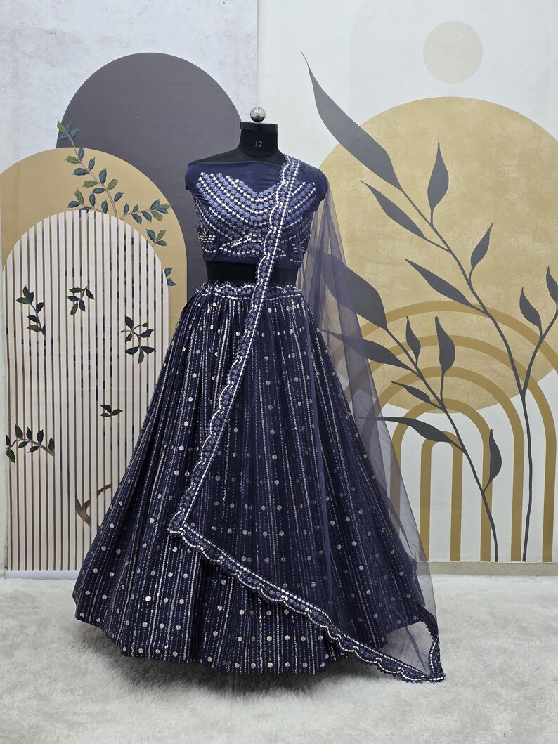May include: Navy blue formal dress with silver embellishments. The two-piece outfit includes a crop top and a long skirt, both adorned with a pattern of vertical lines and scattered dots. A matching sheer scarf drapes over the shoulder.