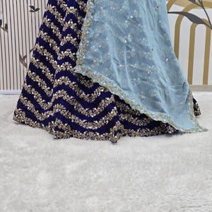 May include: A navy blue skirt with gold and white embroidery and a light blue sheer overlay. The skirt has a wavy pattern and is decorated with sequins.
