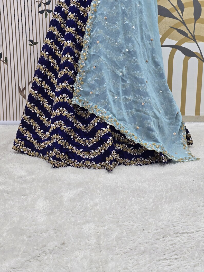 May include: A navy blue skirt with gold and white embroidery and a light blue sheer overlay. The skirt has a wavy pattern and is decorated with sequins.