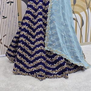 May include: A navy blue skirt with a gold and white embroidered chevron pattern. The skirt is paired with a light blue sheer dupatta.