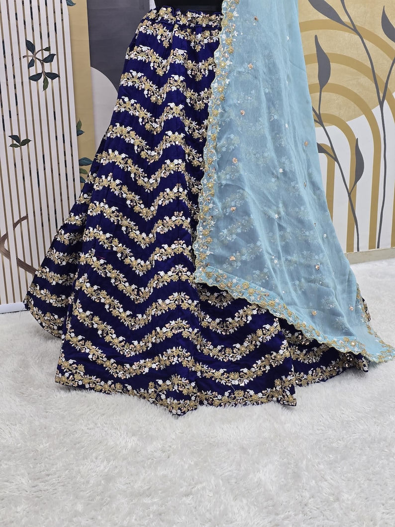 May include: A navy blue skirt with a gold and white embroidered chevron pattern. The skirt is paired with a light blue sheer dupatta.