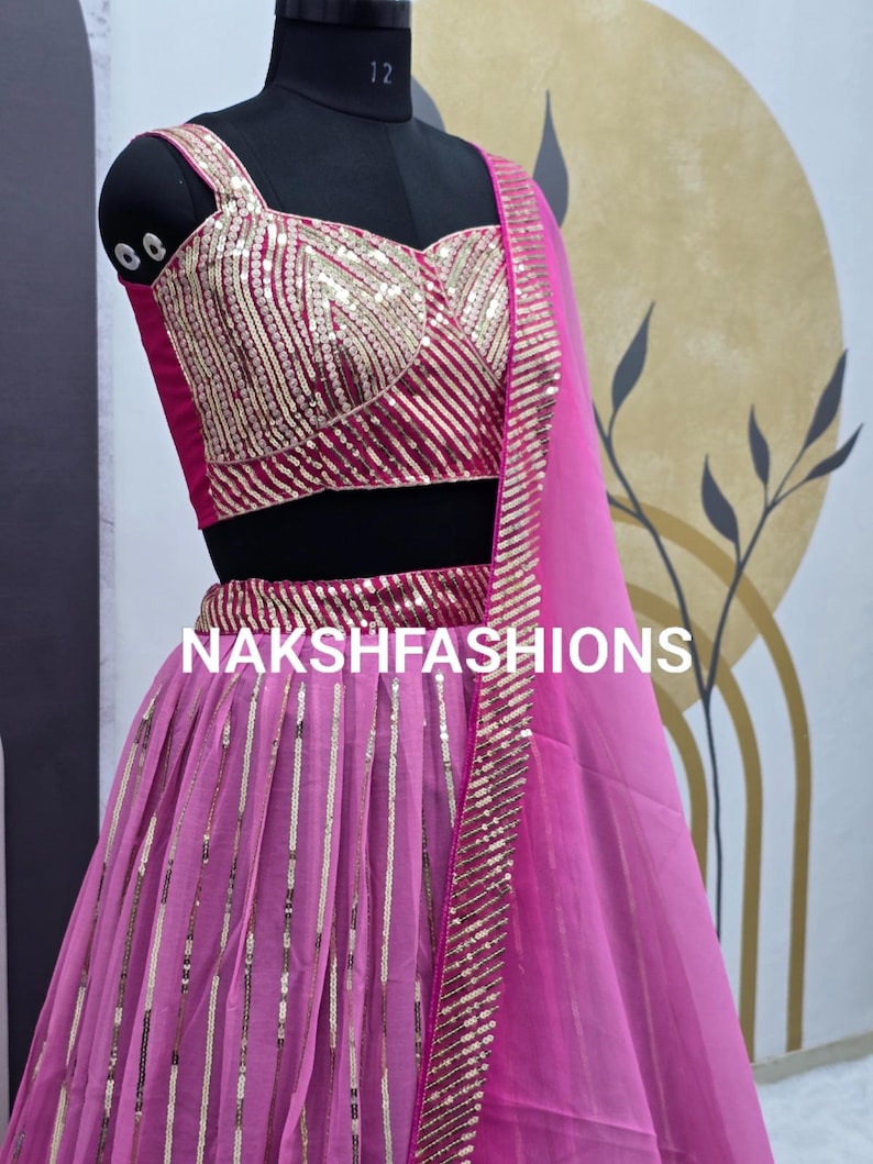 Op de afbeelding: Een roze en gouden pailletten crop top en rok set met een bijpassende, doorschijnende dupatta. De outfit is versierd met gouden pailletten in een gestreept patroon. De tekst "NAKSHFASHIONS" is zichtbaar op de rok.