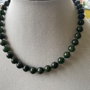 May include: A dark green gemstone necklace with round beads. The necklace is on a white mannequin.