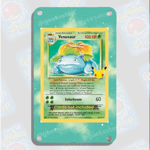 May include: A blue and green Pokemon trading card featuring Venusaur, a Stage 2 Pokemon that evolves from Ivysaur. The card has a light blue background with white stars and a white border. The card's text reads "Venusaur, 100 HP, Seed Pokemon, Length: 6' 7", Weight: 221 lbs. Pokemon Power: Energy Trans As often as you like during your turn (before your attack), you may take 1 Energy card attached to 1 of your Pokemon and attach it to a different one. This power can't be used if Venusaur is Asleep, Confused, or Paralyzed. Solarbeam 60. Cards not included. This plant blooms when it is absorbing solar energy. It stays on the move to seek sunlight. LV.67 #3".