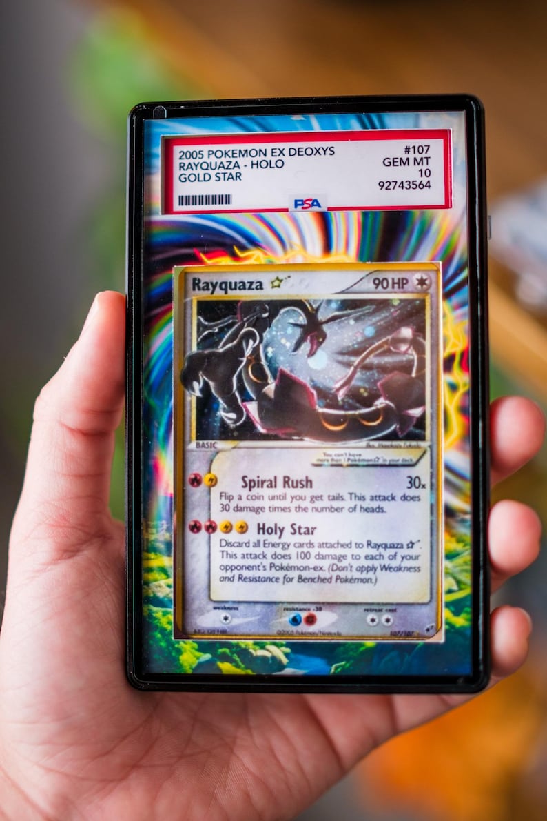 K&ouml;nnte beinhalten: Eine bewertete 2005 Pokemon EX Deoxys Rayquaza Gold Star Karte. Die Karte befindet sich in einer Schutzh&uuml;lle mit einem PSA-Etikett. Die Karte zeigt eine schwarz-gr&uuml;ne Illustration von Rayquaza mit dem Text "Rayquaza" und "90 HP".